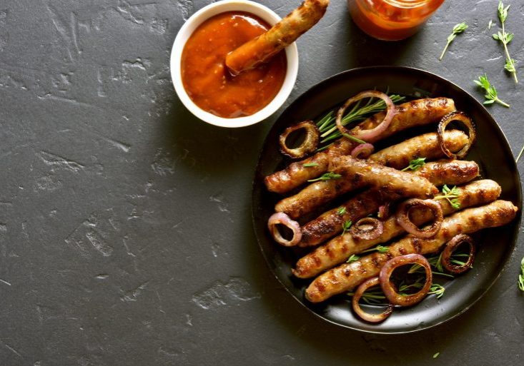 grilled sausages meat with onions and a red sauce on a plate on a dark background