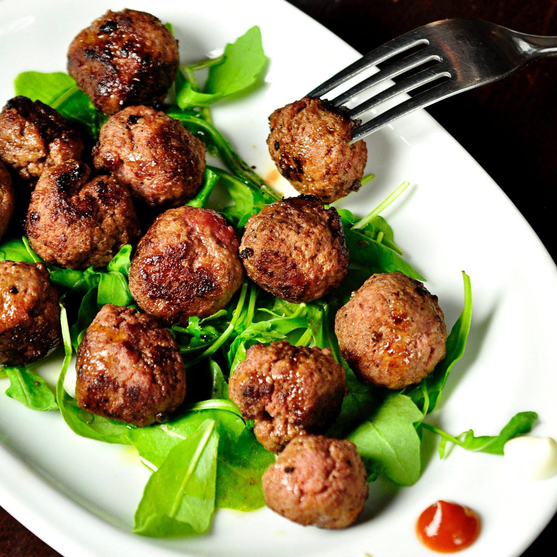 Meatballs with some salad leafs on a white board. Someone pulling a fork in one meatball
