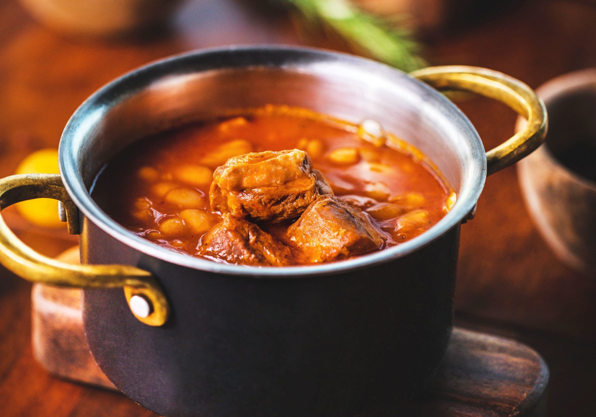 red soup with beans and meat in a pan, standing on a wooden table with rosemary
