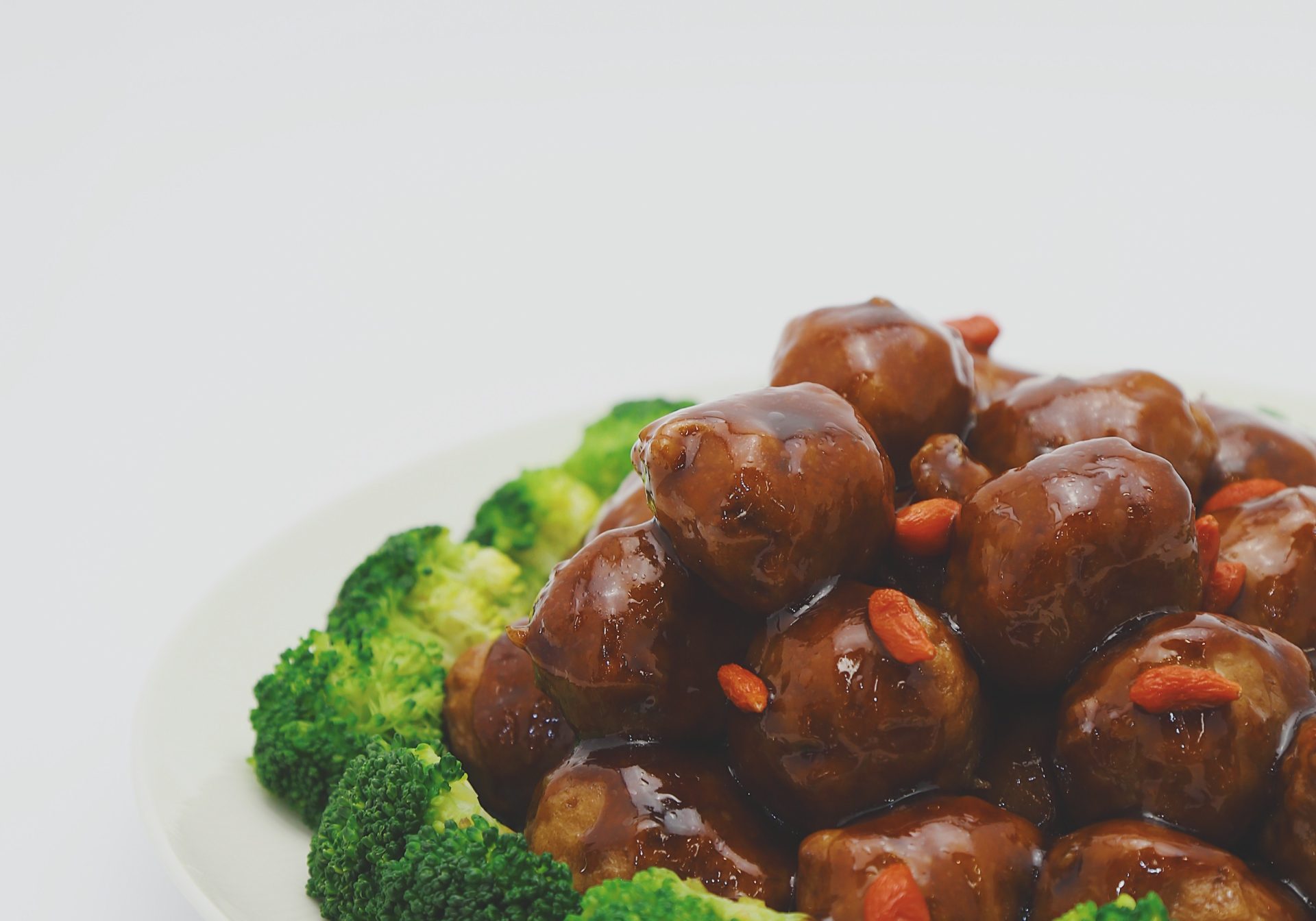Meatballs in sauce with broccoli around it lying on a white plate with white background