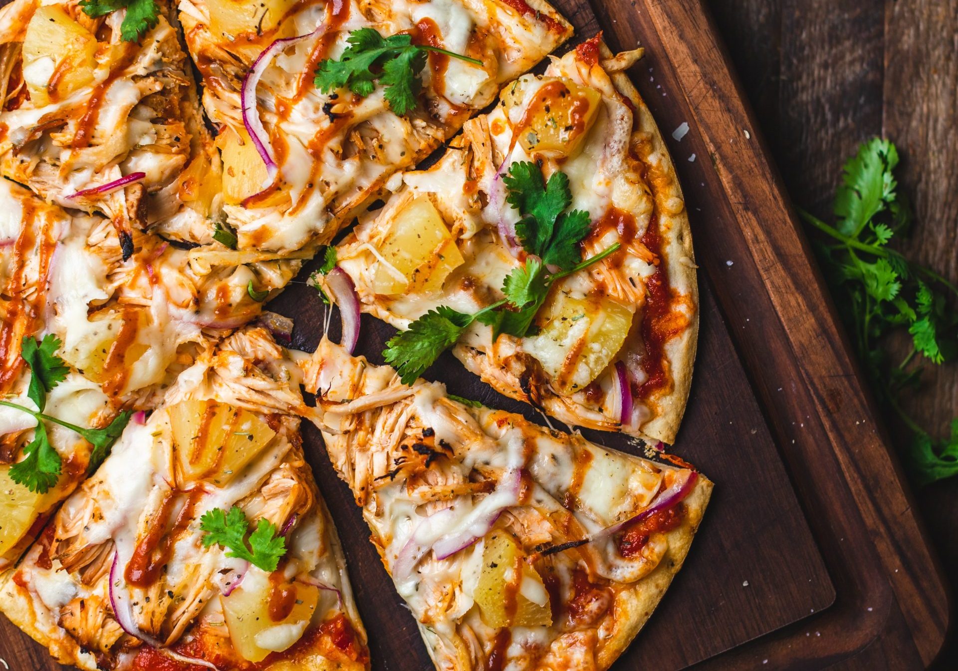 sliced ready meal pizza with some herbs and onions aside on a wooden board on wooden background