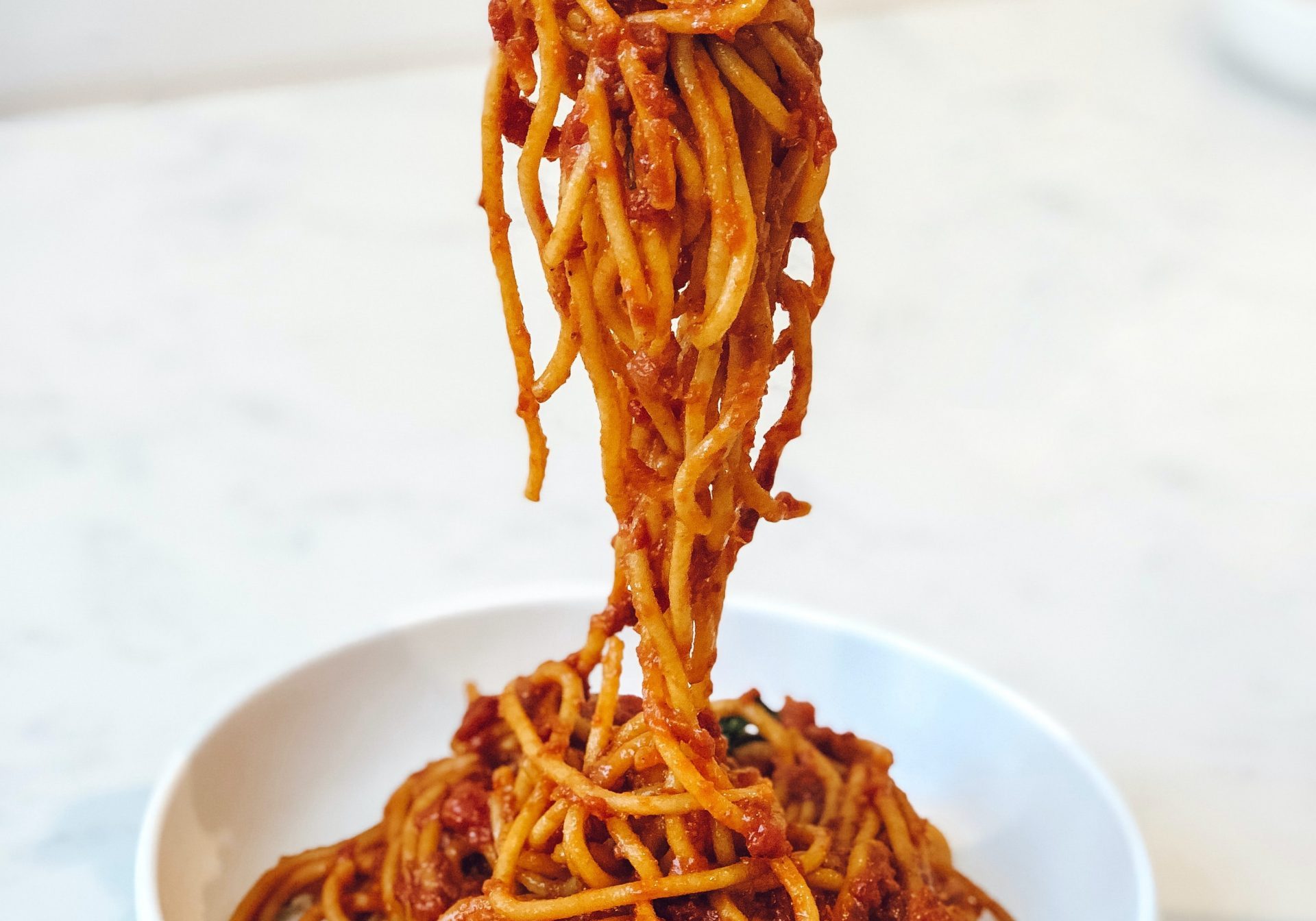 Spaghetti with tomato sauce in a white bowl on white background