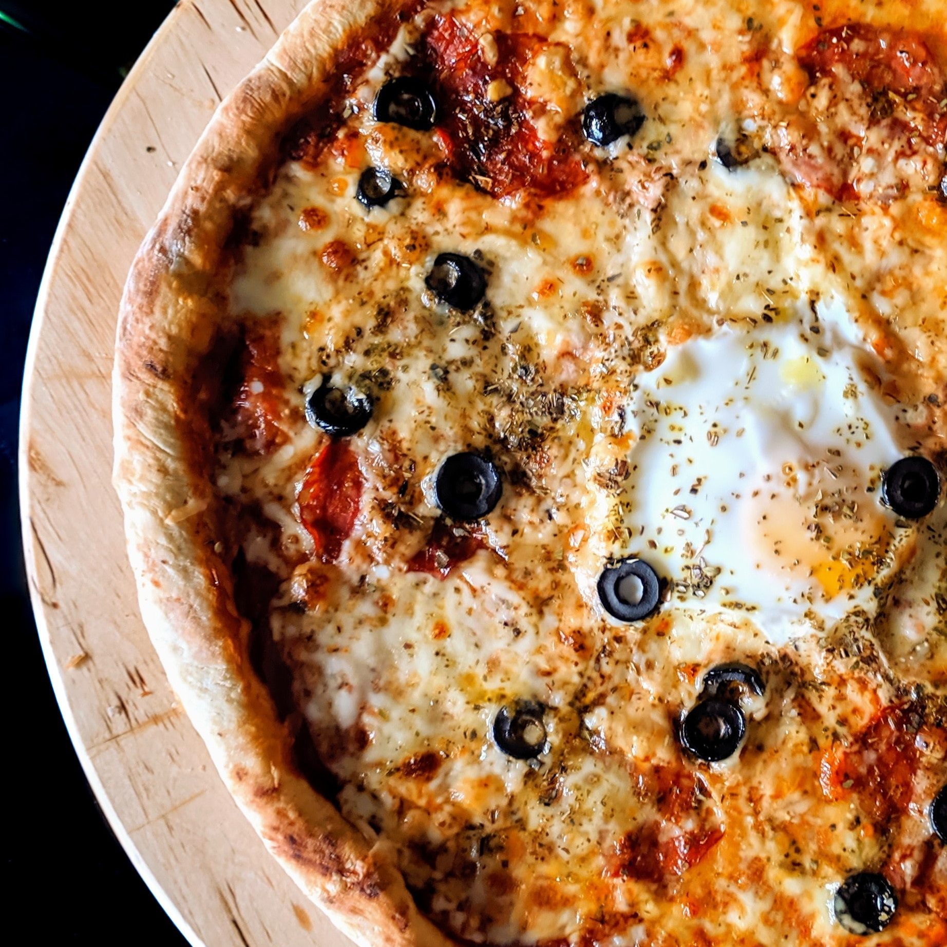 pizza with olives and an egg on a wooden round board on a black background