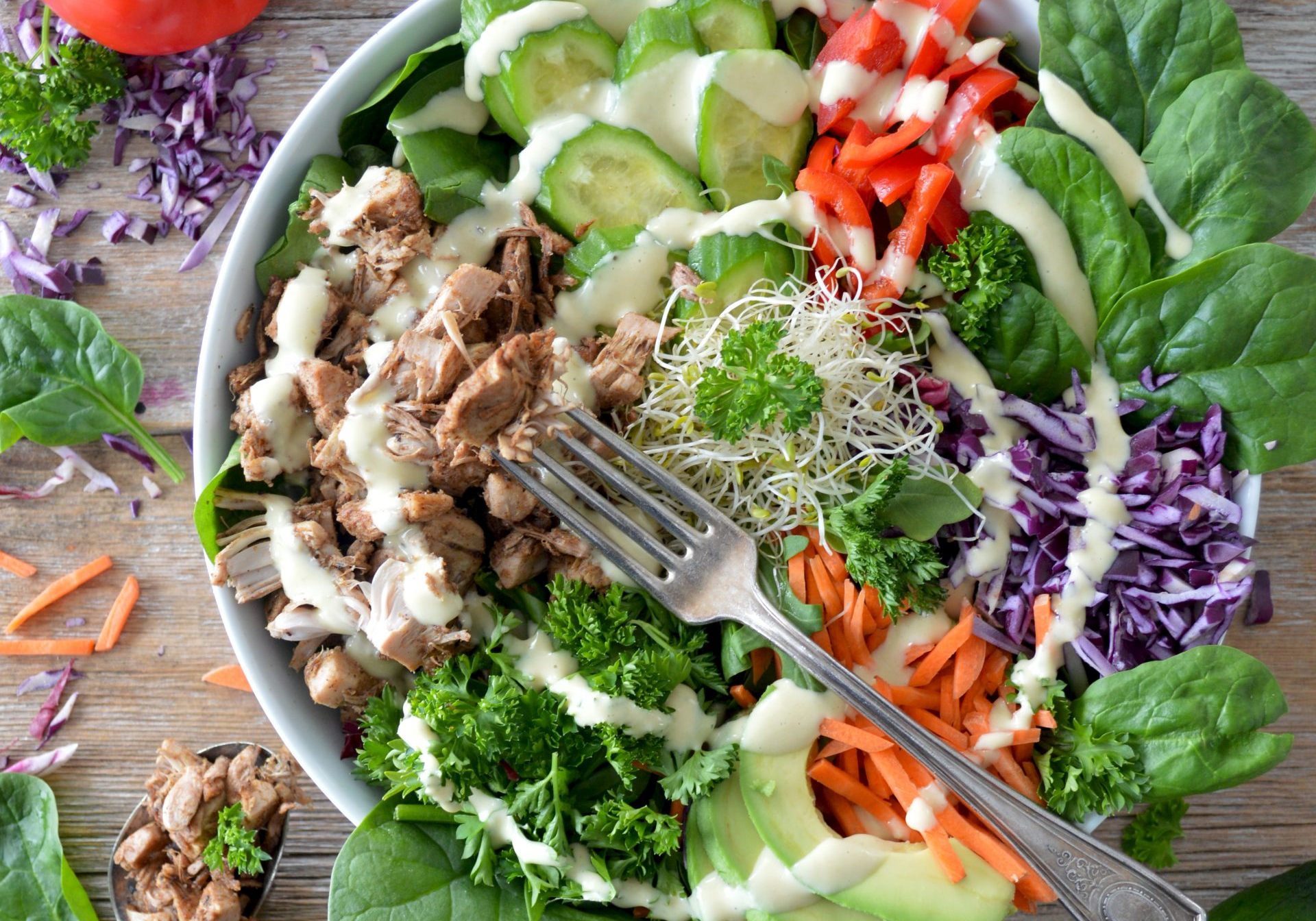 Huge salad bowl with vegetables and meat with dressing on it