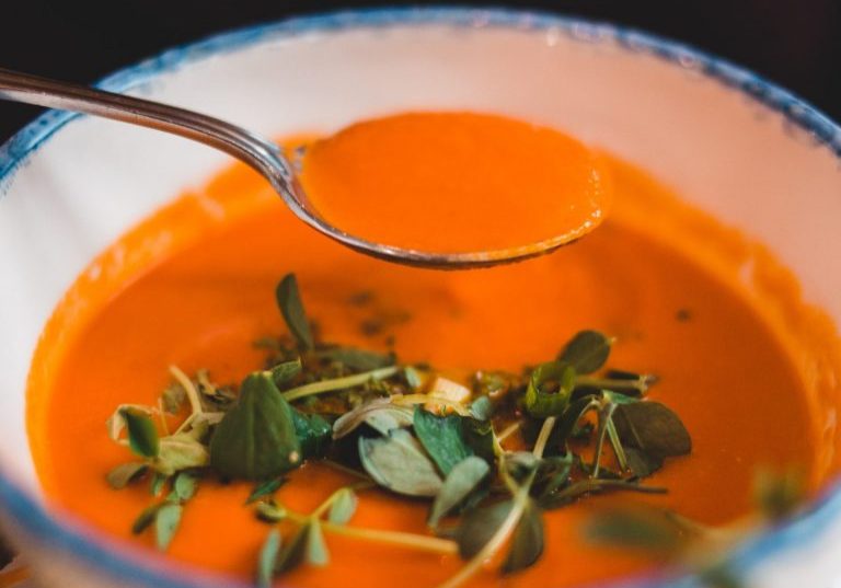 red soup with green herbs in a soup bowl and on a spoon