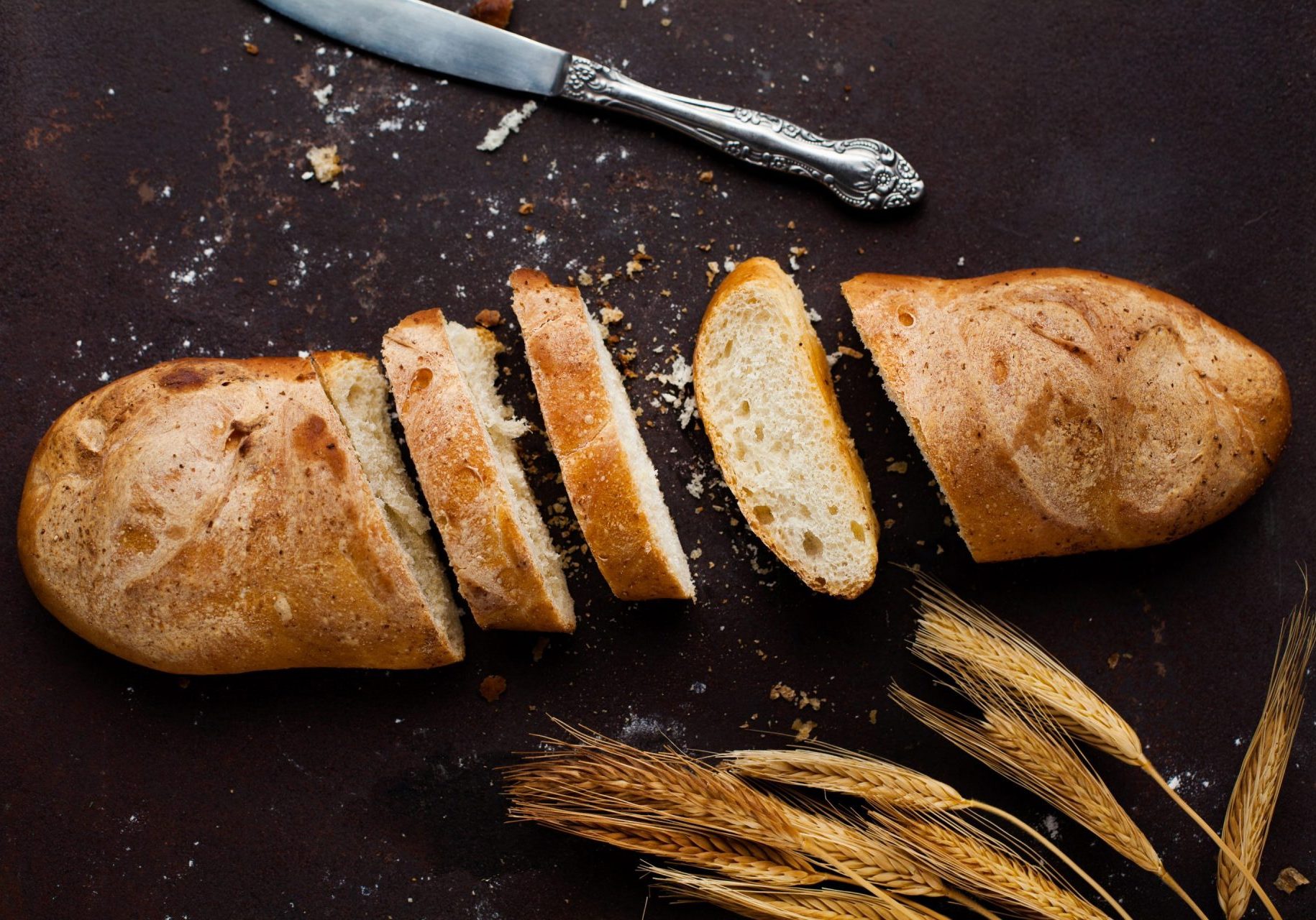 Baking Baguette with three slices and a knife lying on a dark background
