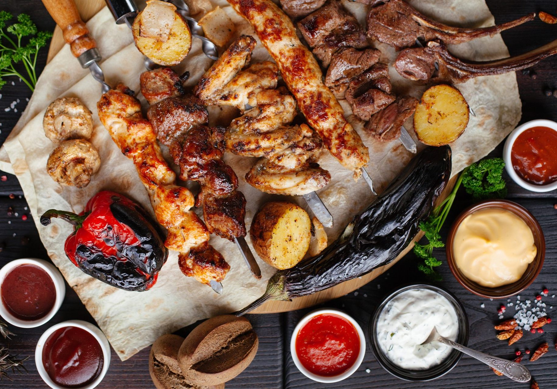 Barbecue meat and sausages with vegetables and dips on a black background