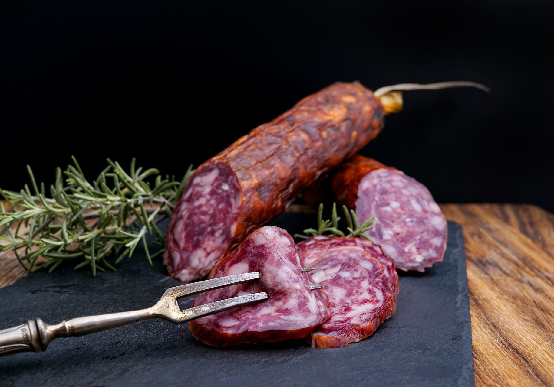 salami cut with rosemary and a fork on a black background